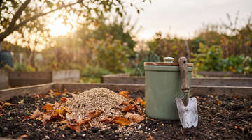 A mound of plant-based cat litter with autumn leaves beside a compost caddy and trowel in a backyard garden