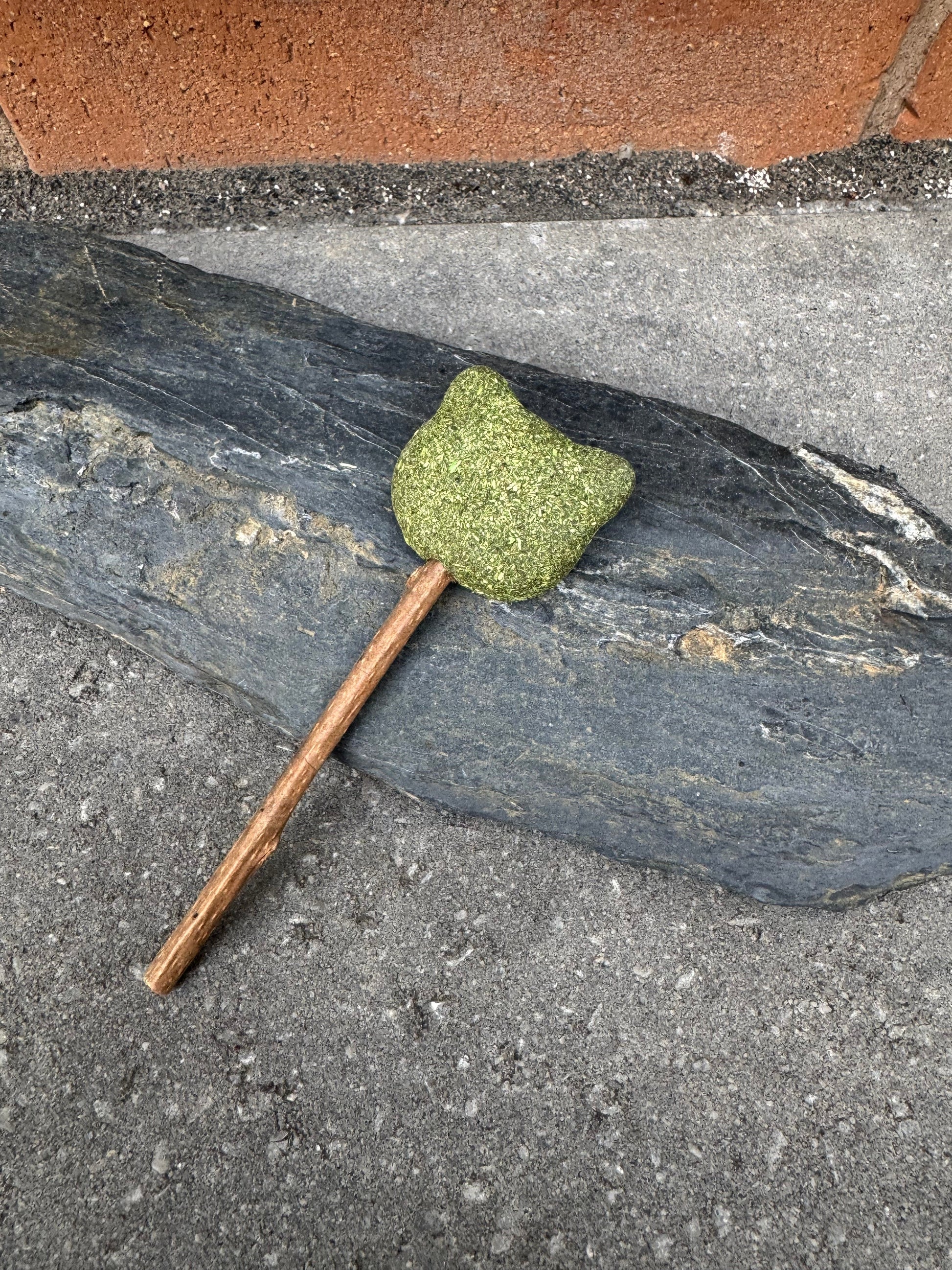 Catnip Lollipop Cat Toy with a cat-head shaped catnip top on a slate slab